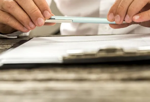 Photo of hands holding a pen over a clipboard with paperwork